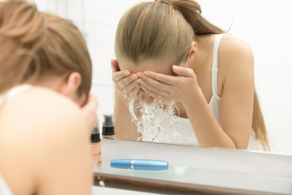 woman washing her face in front of the mirror