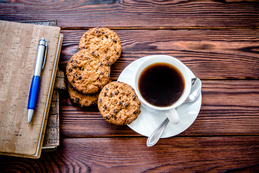A cup of coffee, cookies, a pen, and notebooks