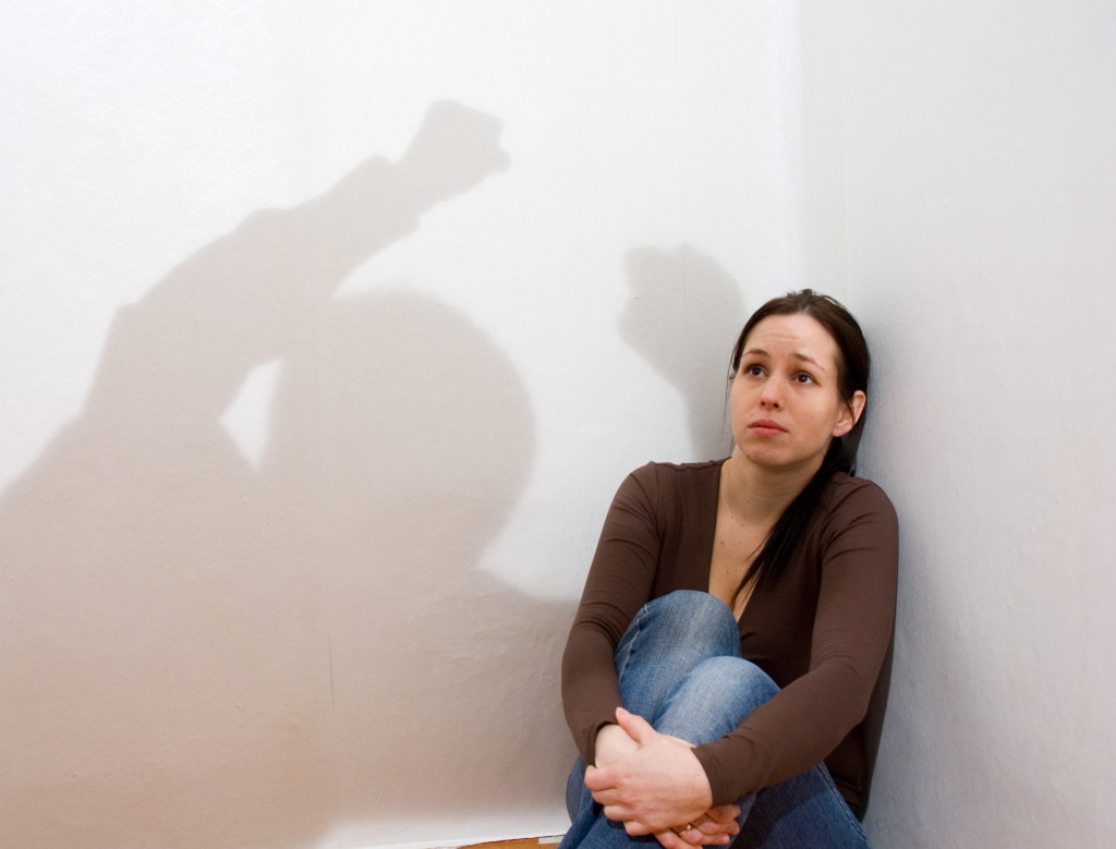 A woman on a corner while the shadow of her violent partner towers over her